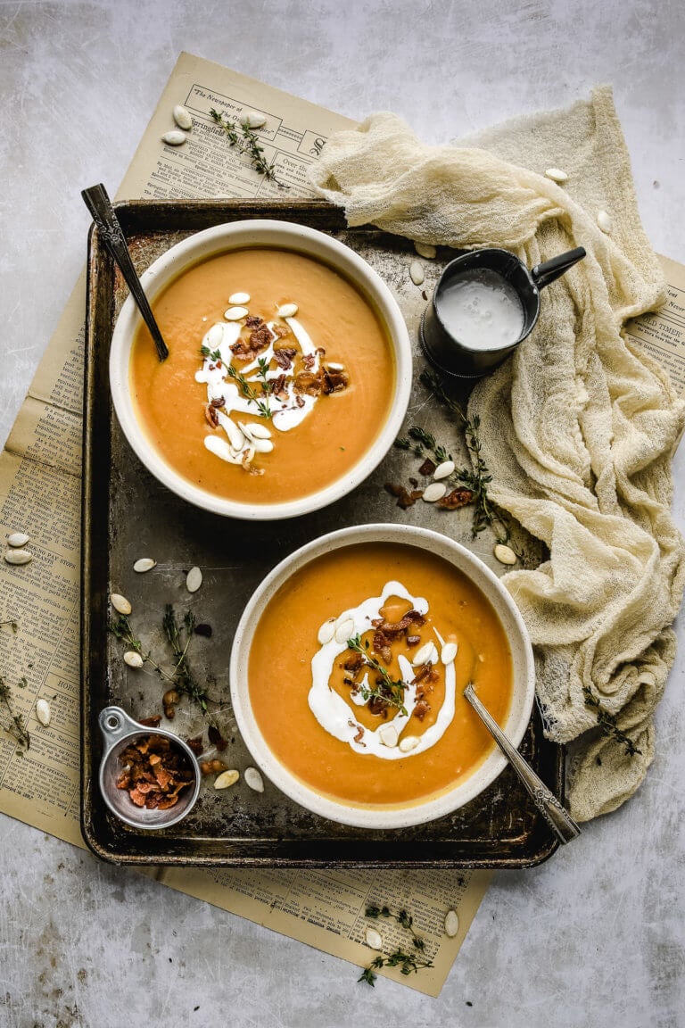 two bowls of squash soup with antique forks on a baking sheet