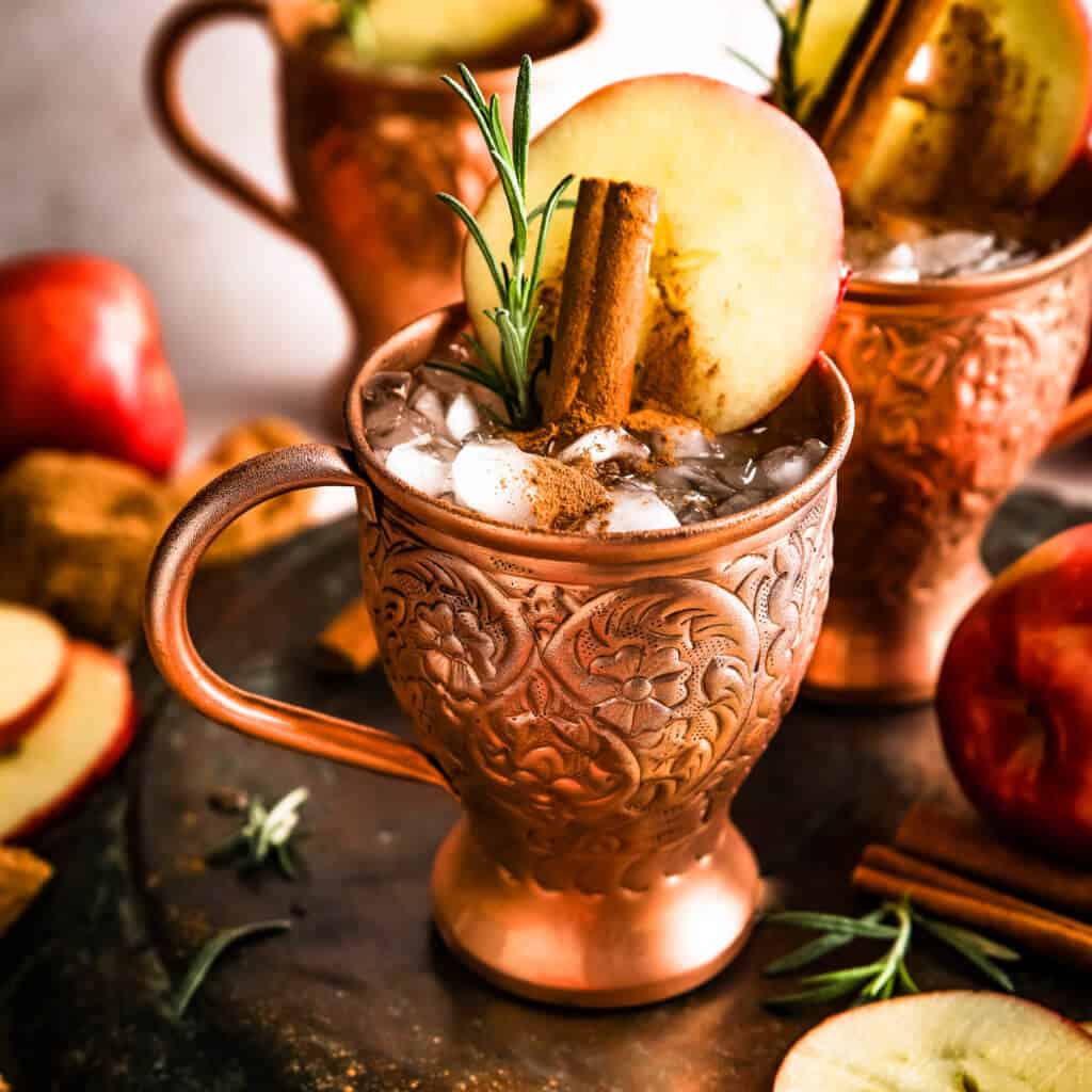 A front shot of the antique copper mug with ice, cinnamon and a apple slice