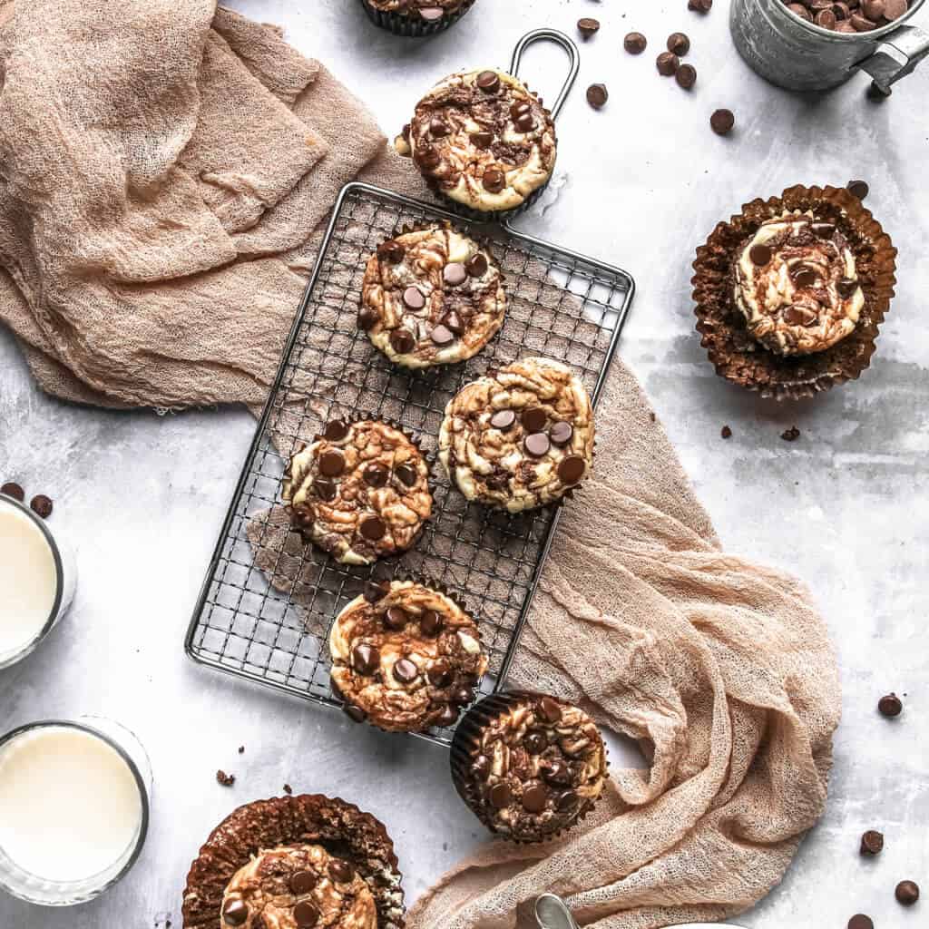 Keto Chocolate Cheesecake Muffins on a cooling rack with chocolate chops and a towel. 