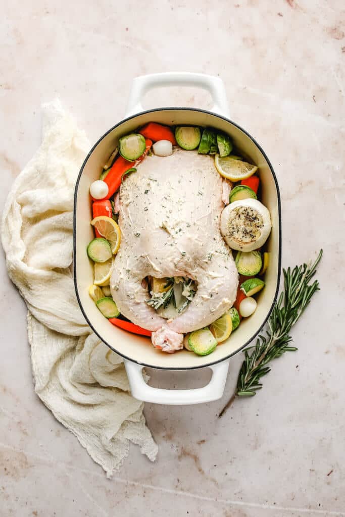 a raw whole chicken over veggies and smothered in herb butter in a dutch oven. 