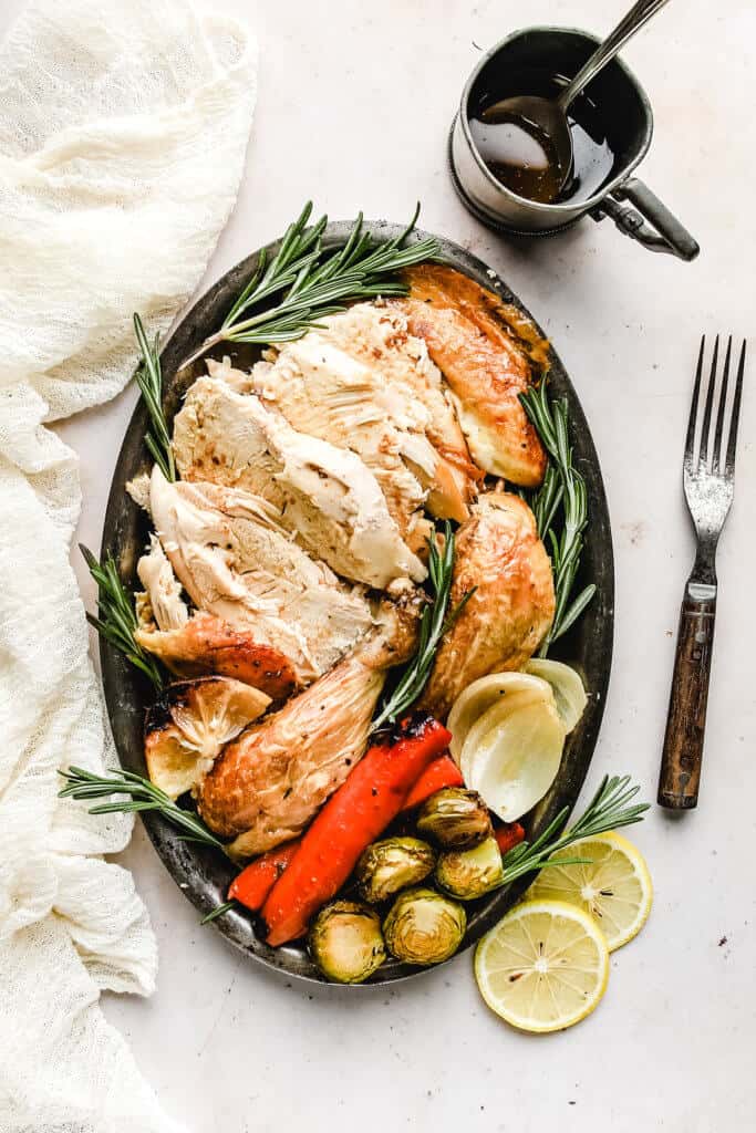 Simple Roast Chicken carved and organized on a platter with roasted veggies, lemon slices and fresh rosemary. 