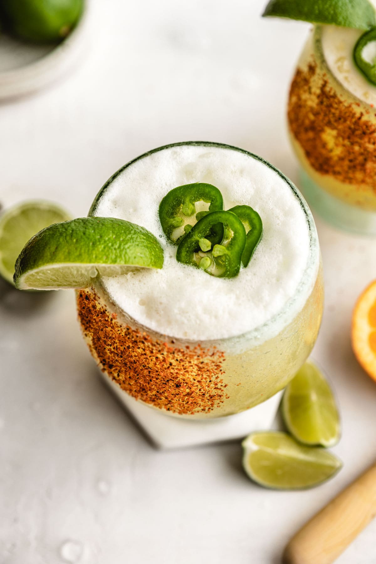 a margarita with a foamy top and a tajin rim topped with freshly sliced jalapenos and a lime wedge.