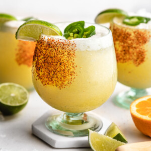 a spicy margarita in a glass with a tajin rim and garnished with a lime jalapeño.