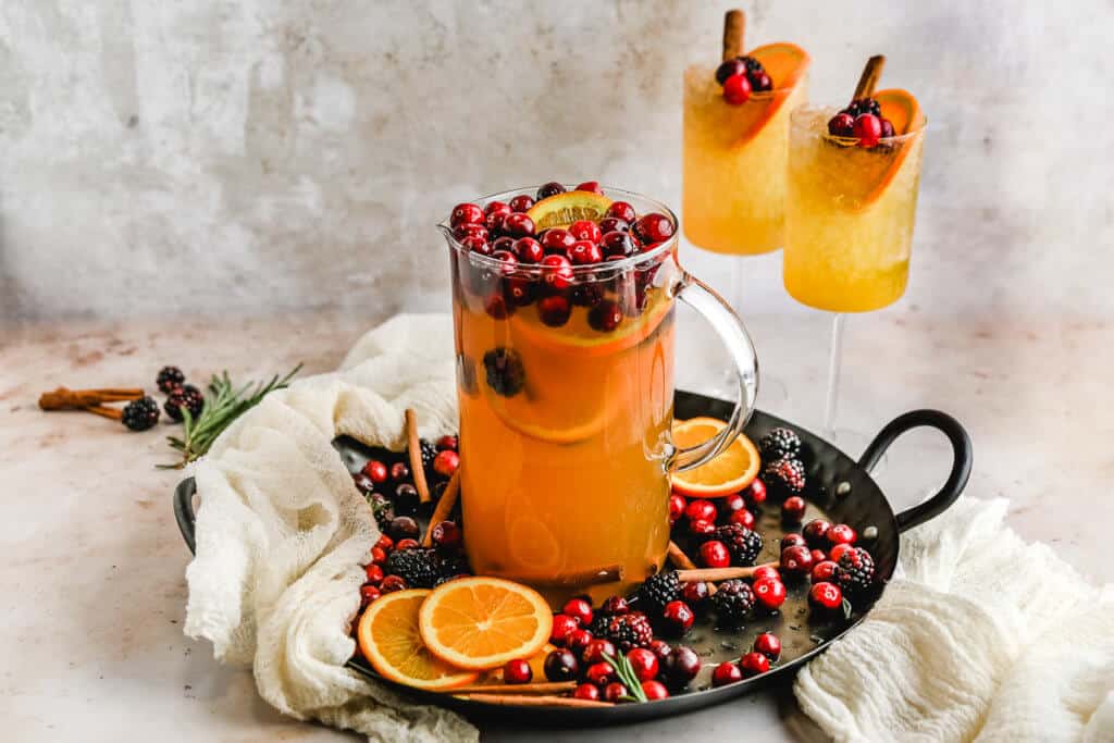 A large pitcher of fall punch filled with orange slices, cranberries and cinnamon sticks