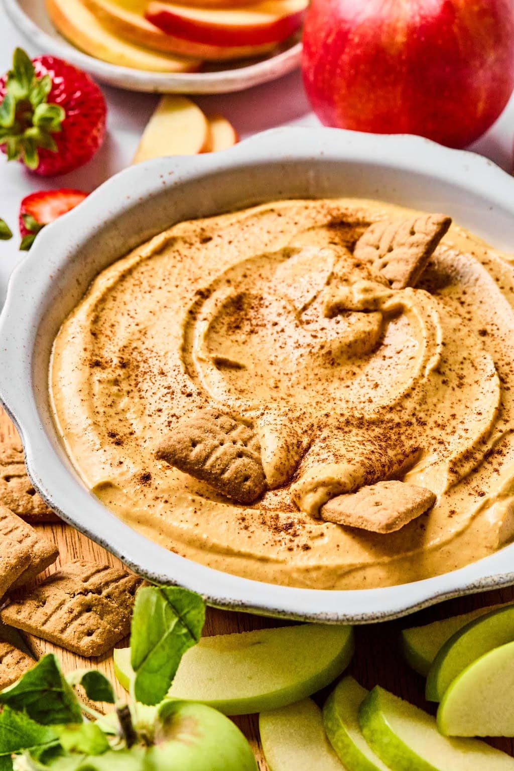 Chilled pumpkin dip recipe dusted with cinnamon in a serving bowl with fruit and cookies for dipping.