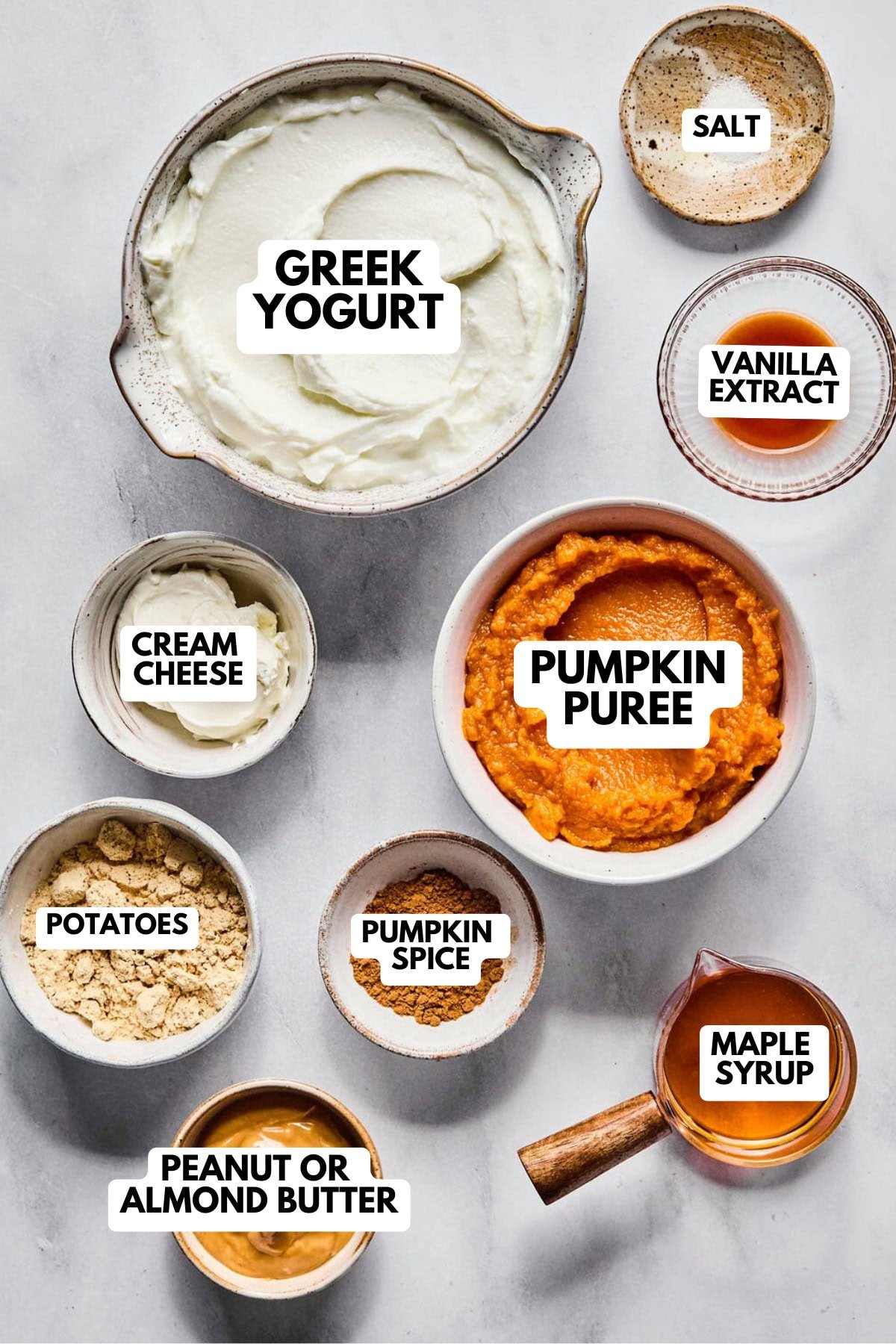 Overhead of pumpkin dip ingredients: pumpkin purée, yogurt, cream cheese, peanut butter, protein powder, maple syrup, and spices.