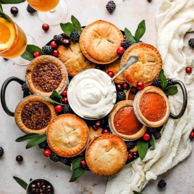 an overhead shot of a dessert charcuterie board filled with mini pie and a bowl of whipped cream.