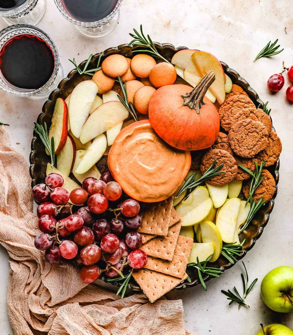 A large platter filled with pumpkin dip in a hollowed out pumpkin, grapes, apple slices, graham crackers, ginger snaps and vanilla wafers