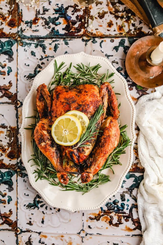 air fryer whole chicken topped with lemon slices and fresh rosemary on a white serving platter.