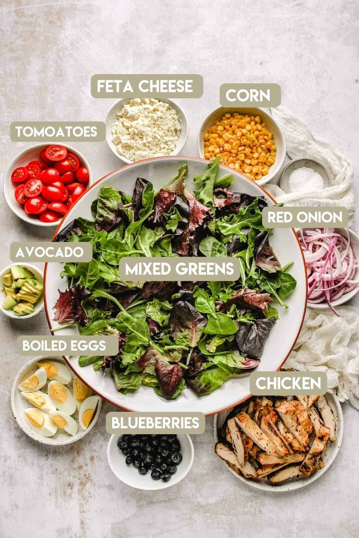 recipe ingredients labeled in small bowls around a big bowl of mixed salad greens