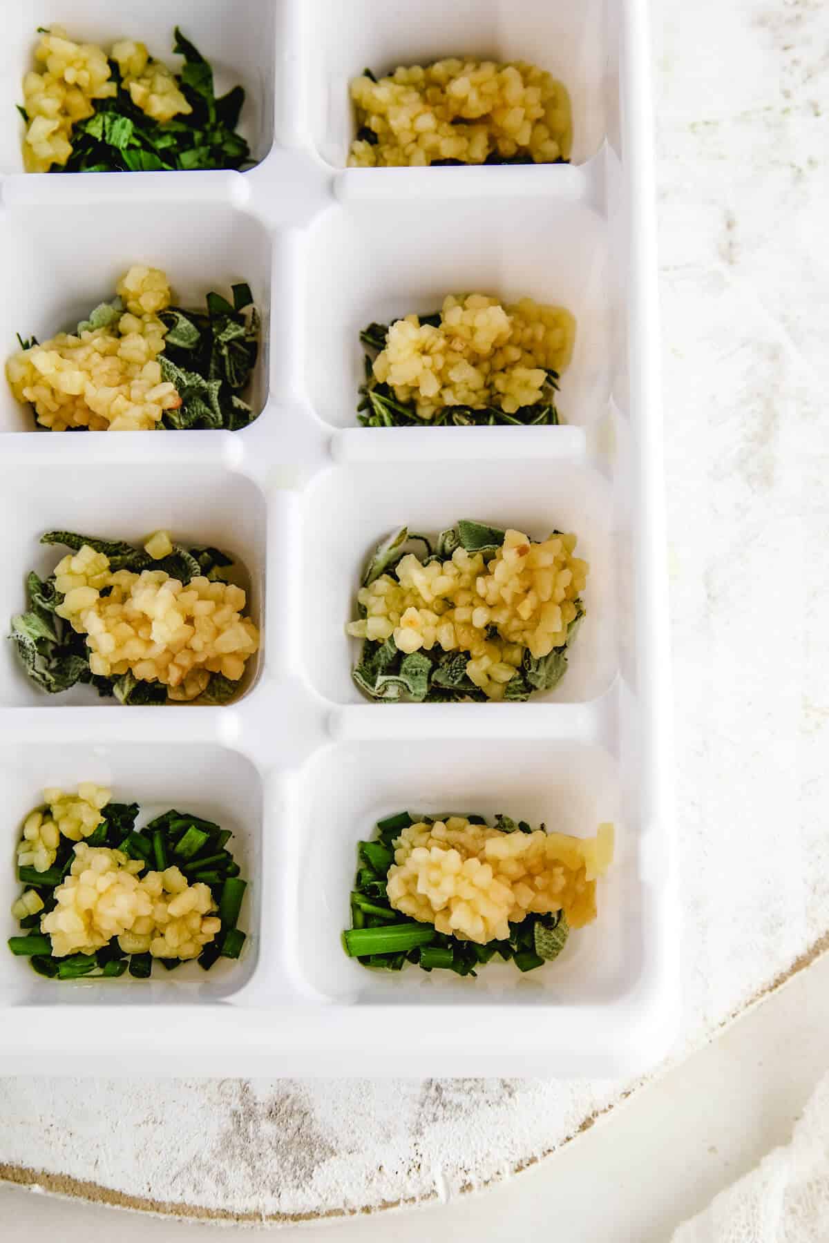 a close up image of minced garlic on top of fresh herbs chopped and placed in a white ice cube tray