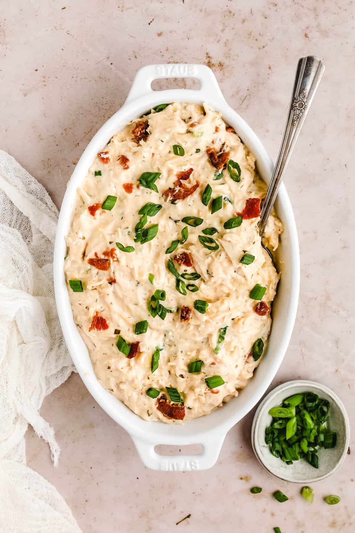 a oval baking dish filled with the creamy Crockpot Ranch Chicken and topped with bacon and green onions