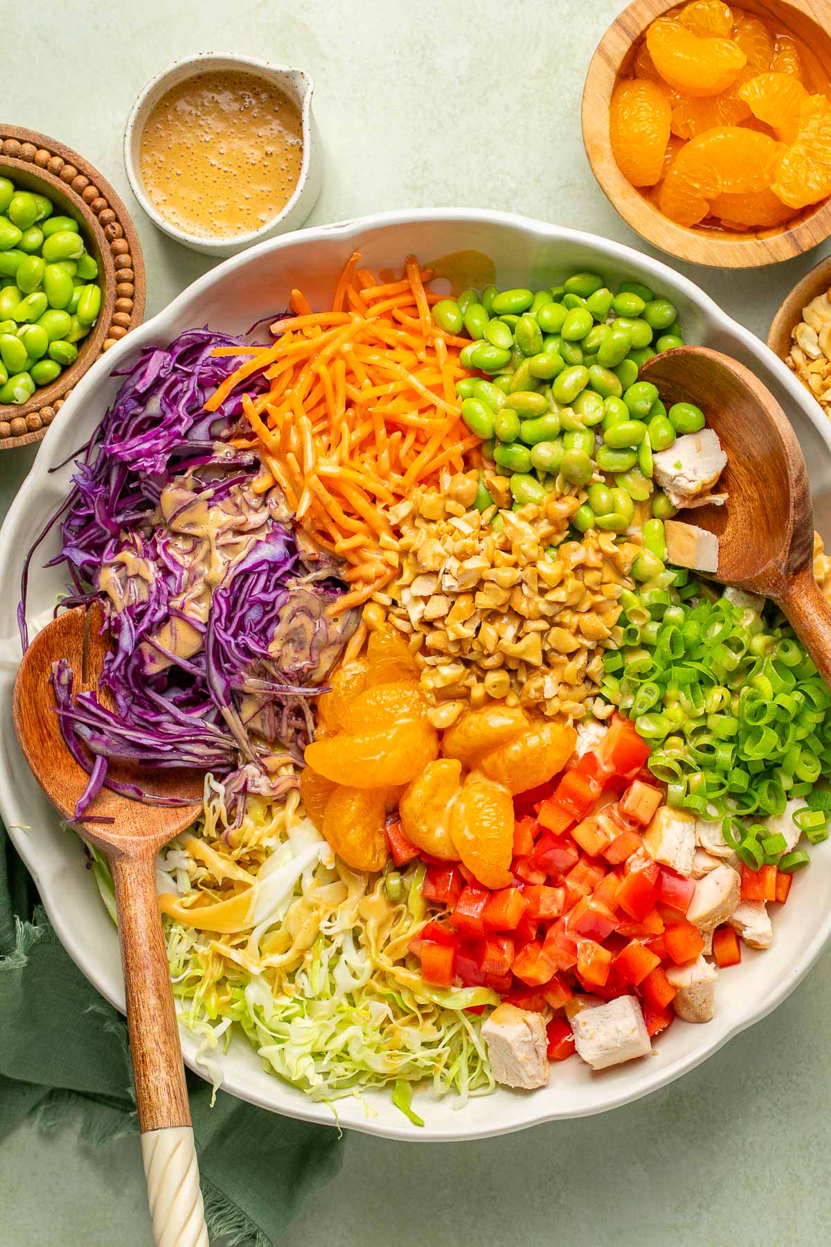 an unmixed Asian chopped salad in a white salad bowl with wooden tongs