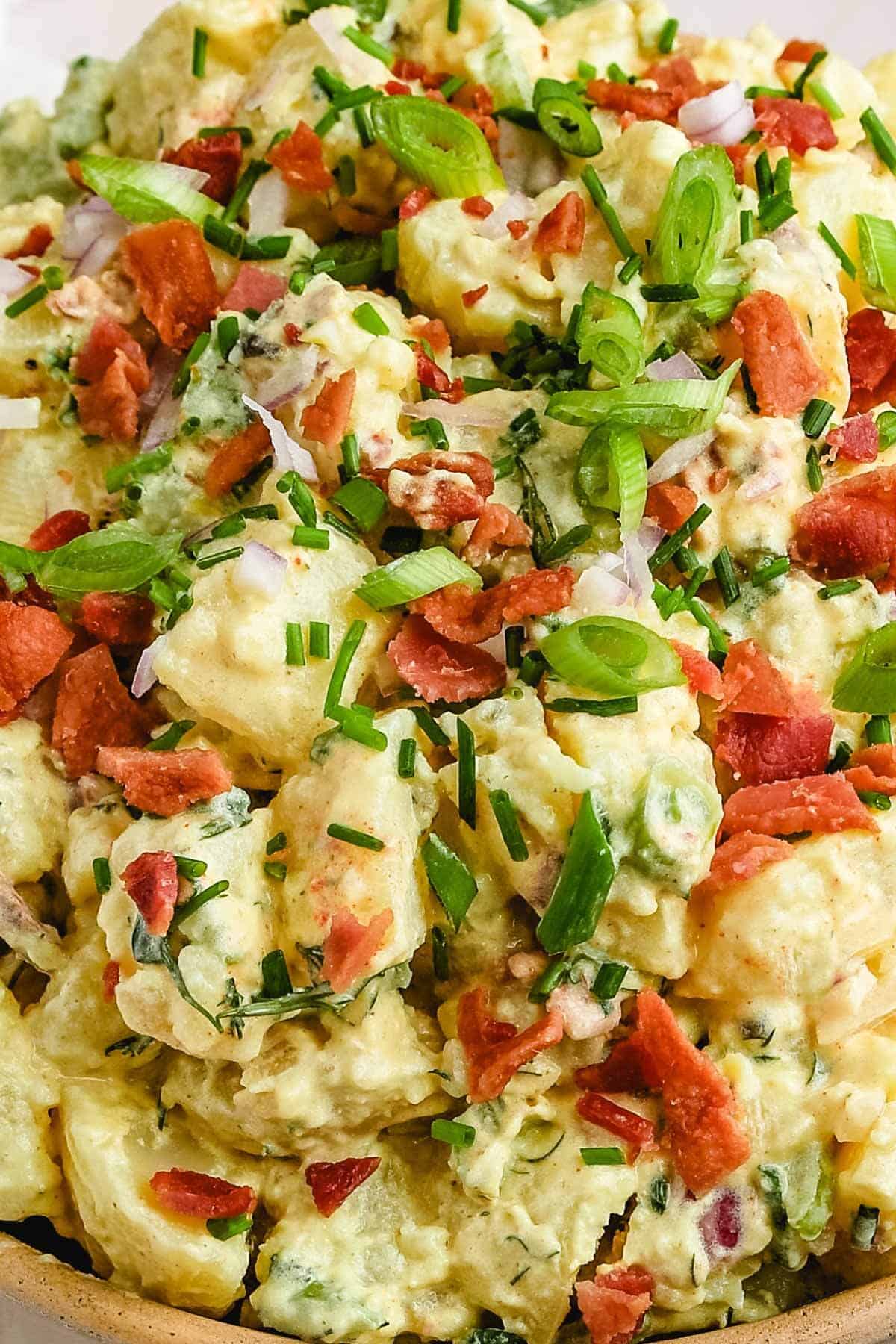a closeup of potato salad with fresh chives, chopped bacon, and diced green onions. 