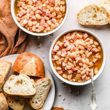 two bowls of instant pot ham and beans soup next to a plate of sliced bread