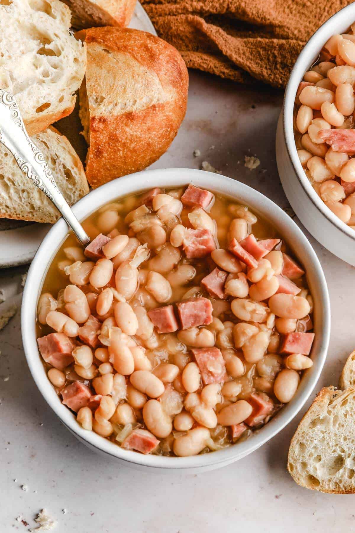 a close up of a white bowl filled with ham and beans recipe with a silver spoon resting agains the bowl