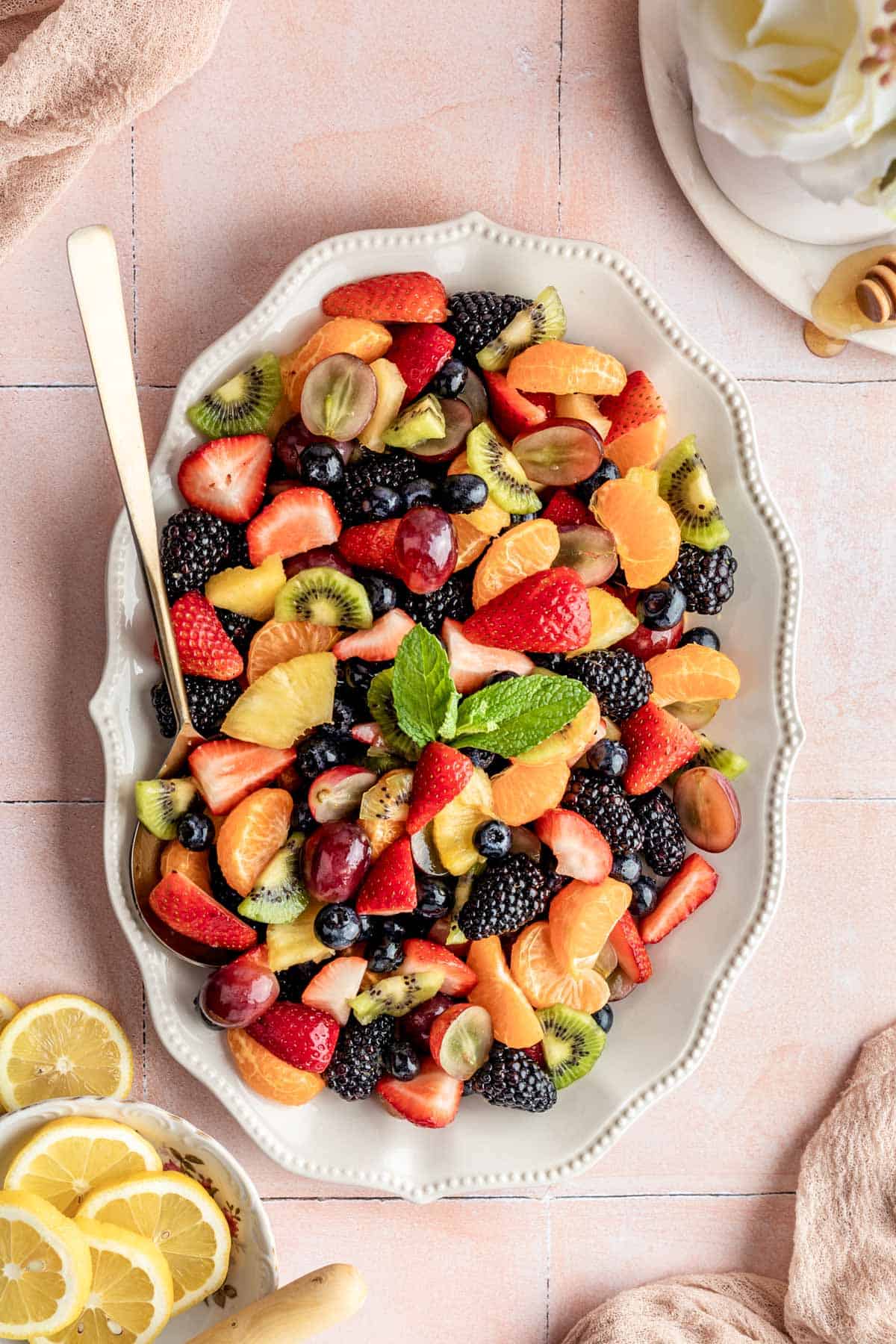 a large white dish filled with fruit salad with a gold spoon resting on the side