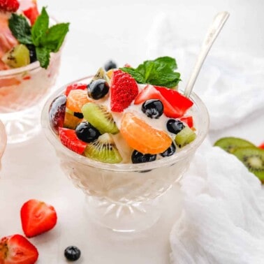a glass bowl filled with fruit salad with ice cream with a spoon resting on the side