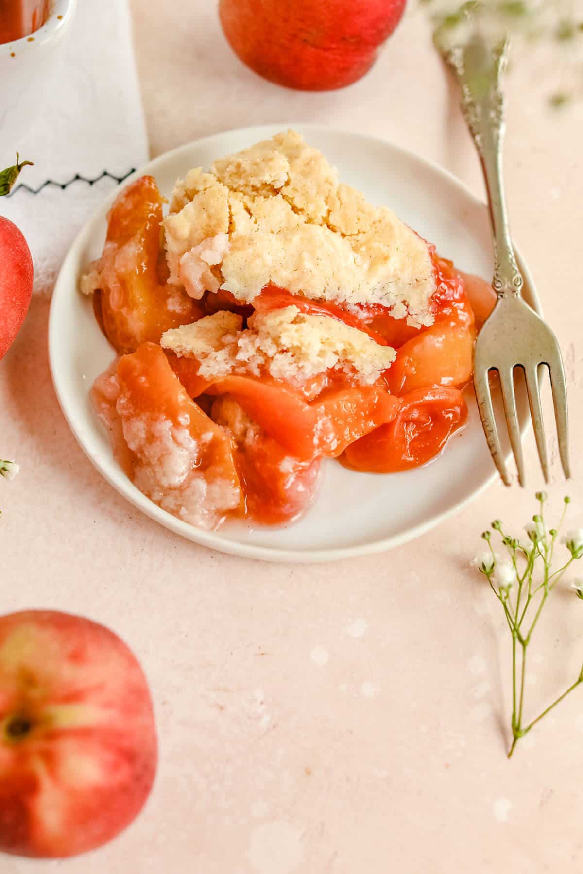 a closeup of a slice of vegan peach cobbler on a white plate with a crumble topping