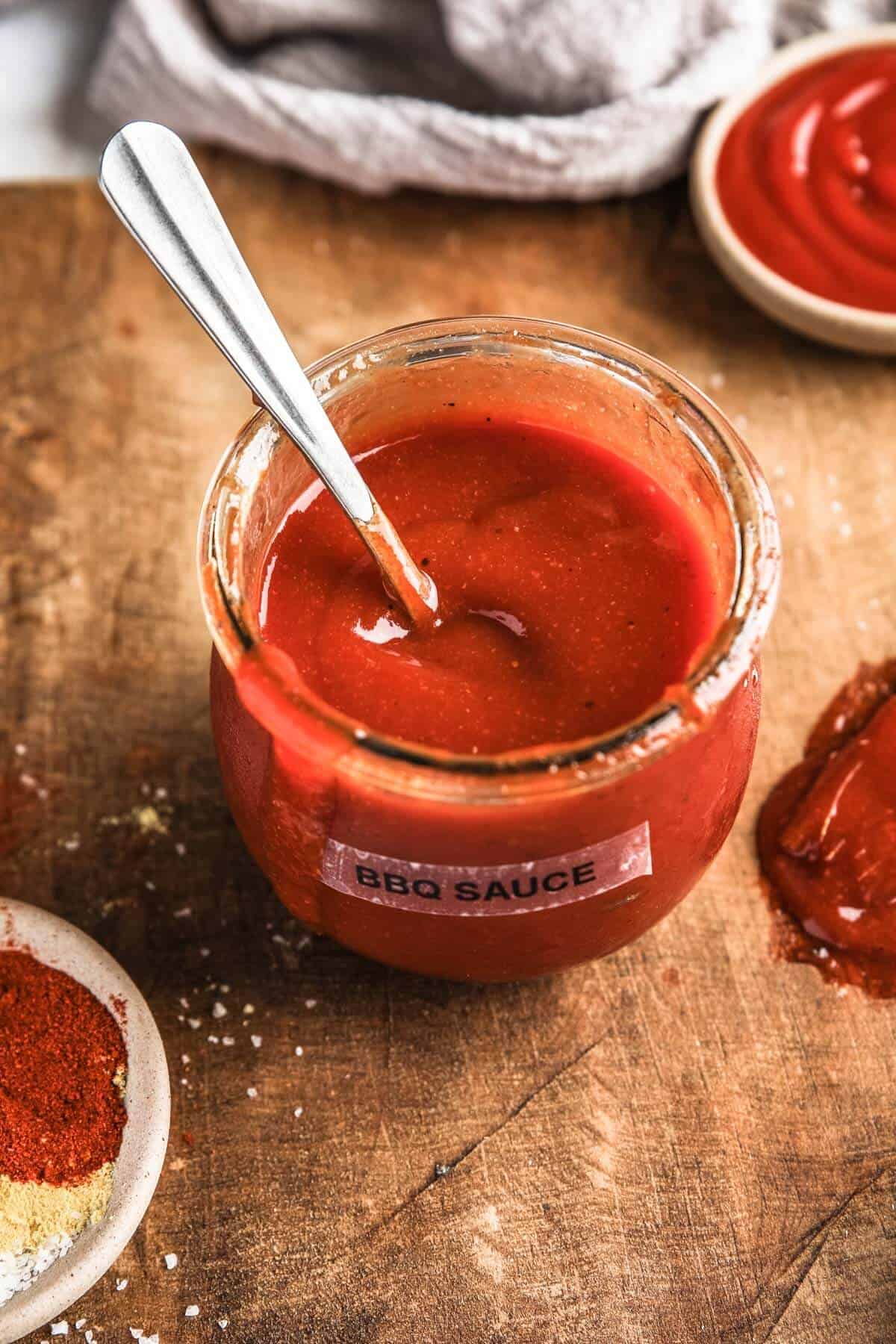 a small glass jar labeled "bbq sauce" with a silver spoon resting inside