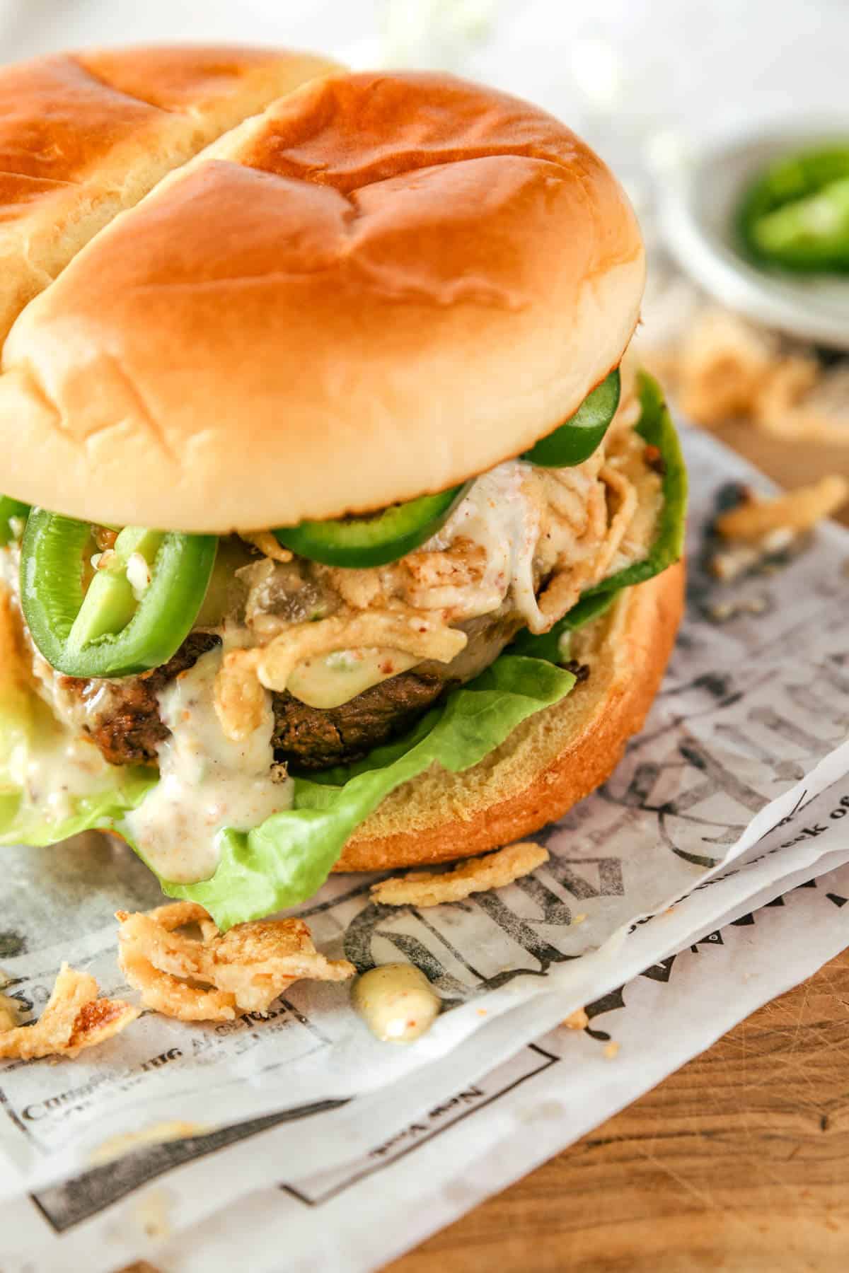 a zoomed in photo of jalapeno cheeseburgers with crispy onions, bacon aioli, and jalapenos. 
