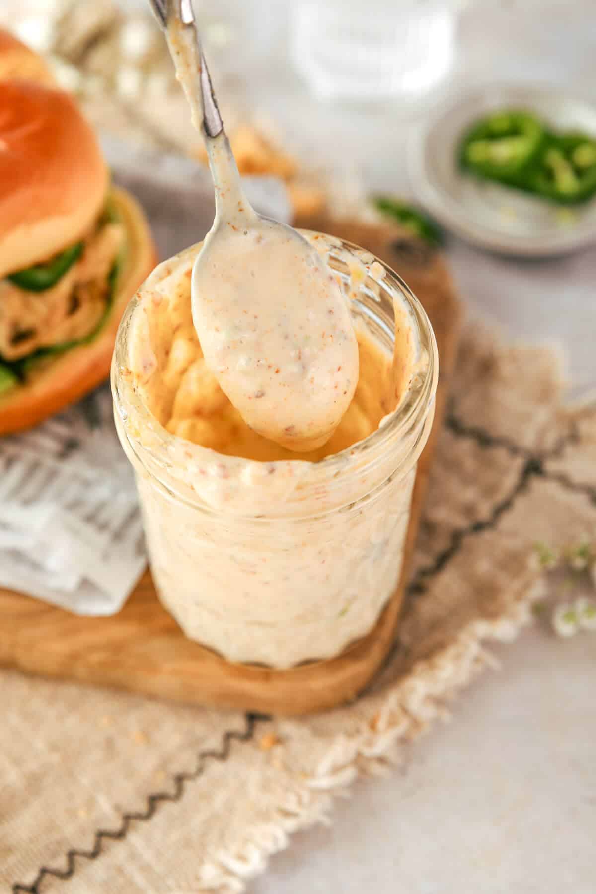 a silver spoon being held over the top of a small glass mason jar filled with bacon aioli