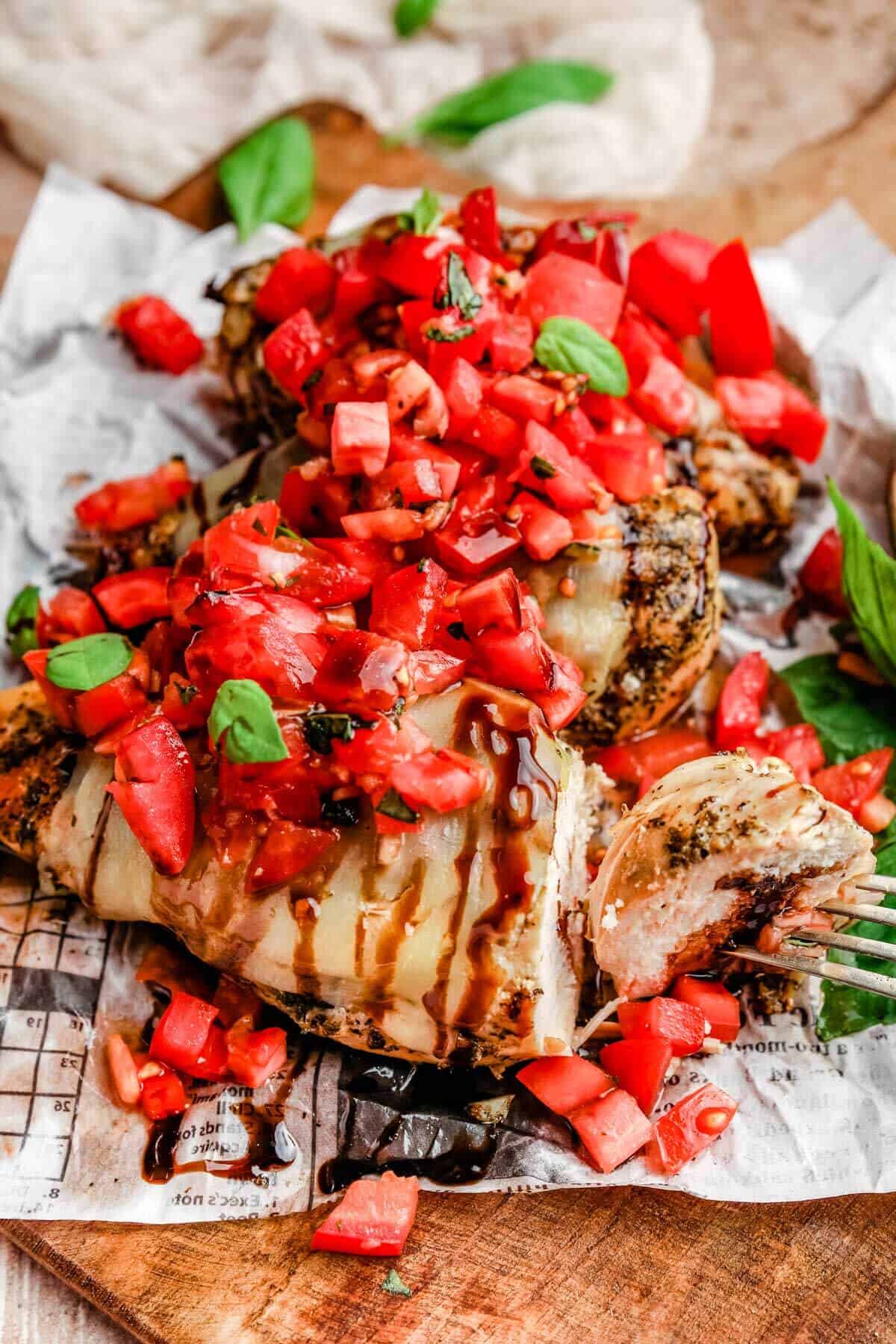 a close up of grilled bruschetta chicken with a fork taking out one bite to show the tender chicken breast