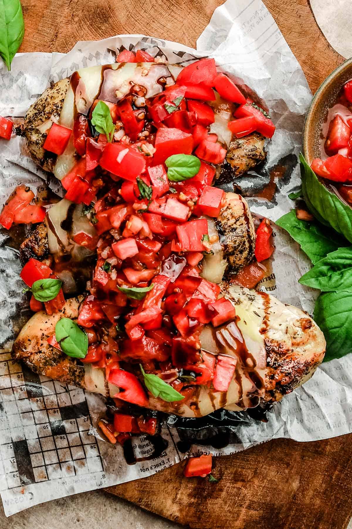 a close up of three chicken breasts topped with bruschetta tomatoes and fresh basil