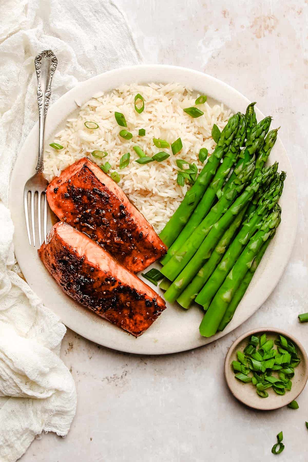 an overhead shot of a white plate with two salmon filets, asparagus and rice with a silver fork. 