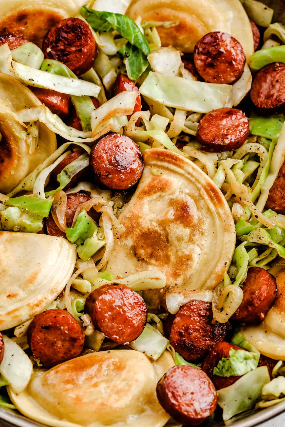 a close-up shot of cabbage and sausage skillet with pierogis in a stainless steel skillet