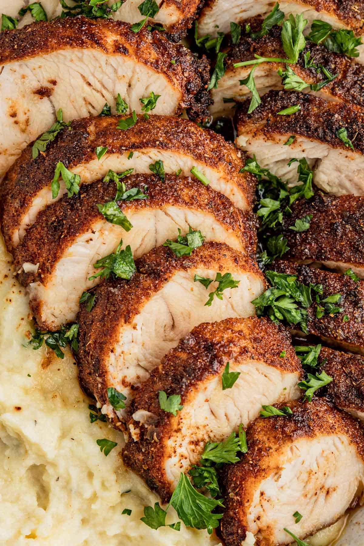 a close up of turkey tenderloins topped with fresh parsley next to mashed potatoes