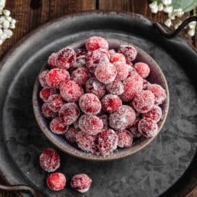 a bowl of candied cranberries resting on a black rustic platter