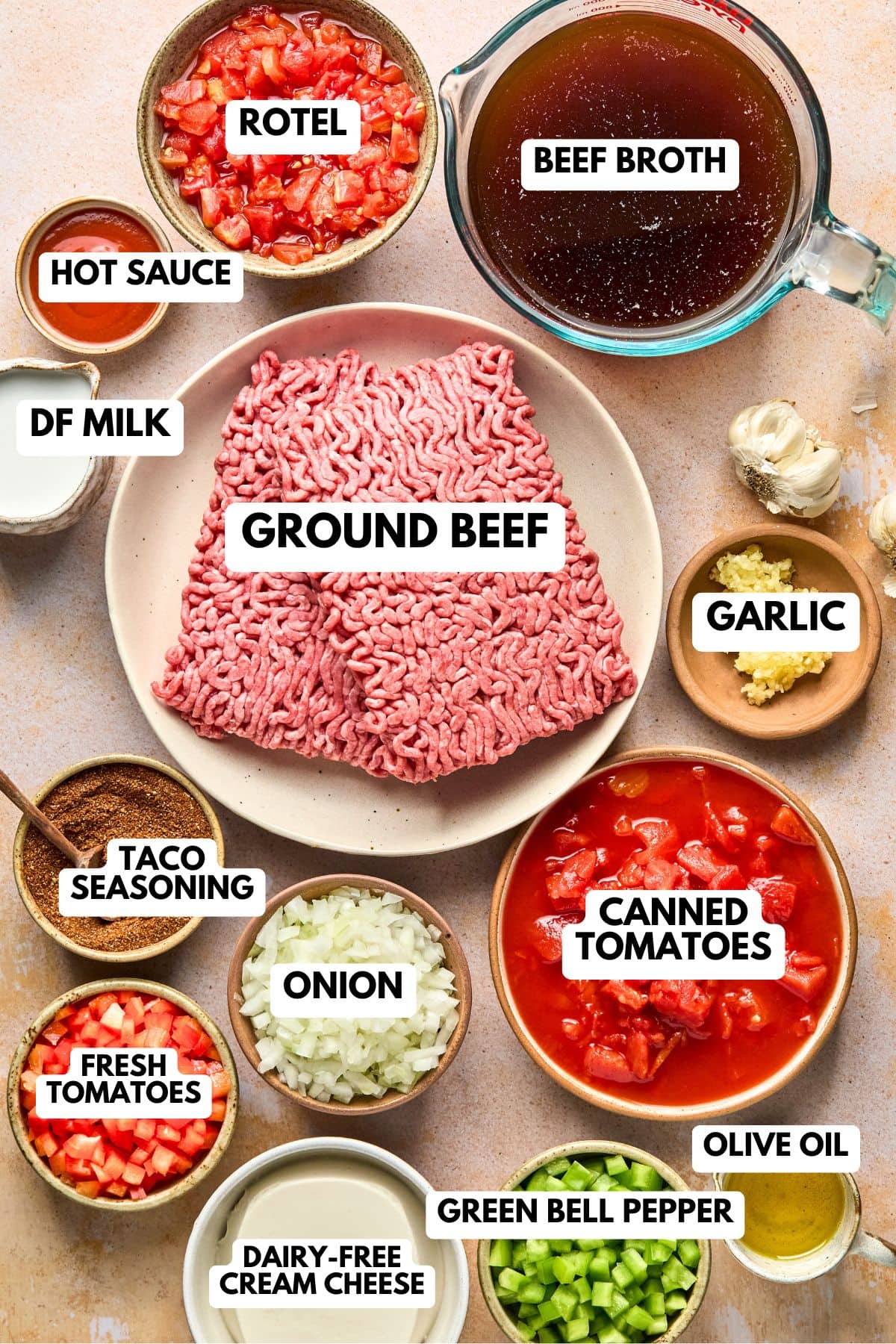 Ingredients for creamy taco soup arranged on a counter including, ground beef, peppers, onion, tomatoes, Rotel tomatoes, broth, spices, coconut milk, cream cheese, garlic, dairy-free milk, and hot sauce.