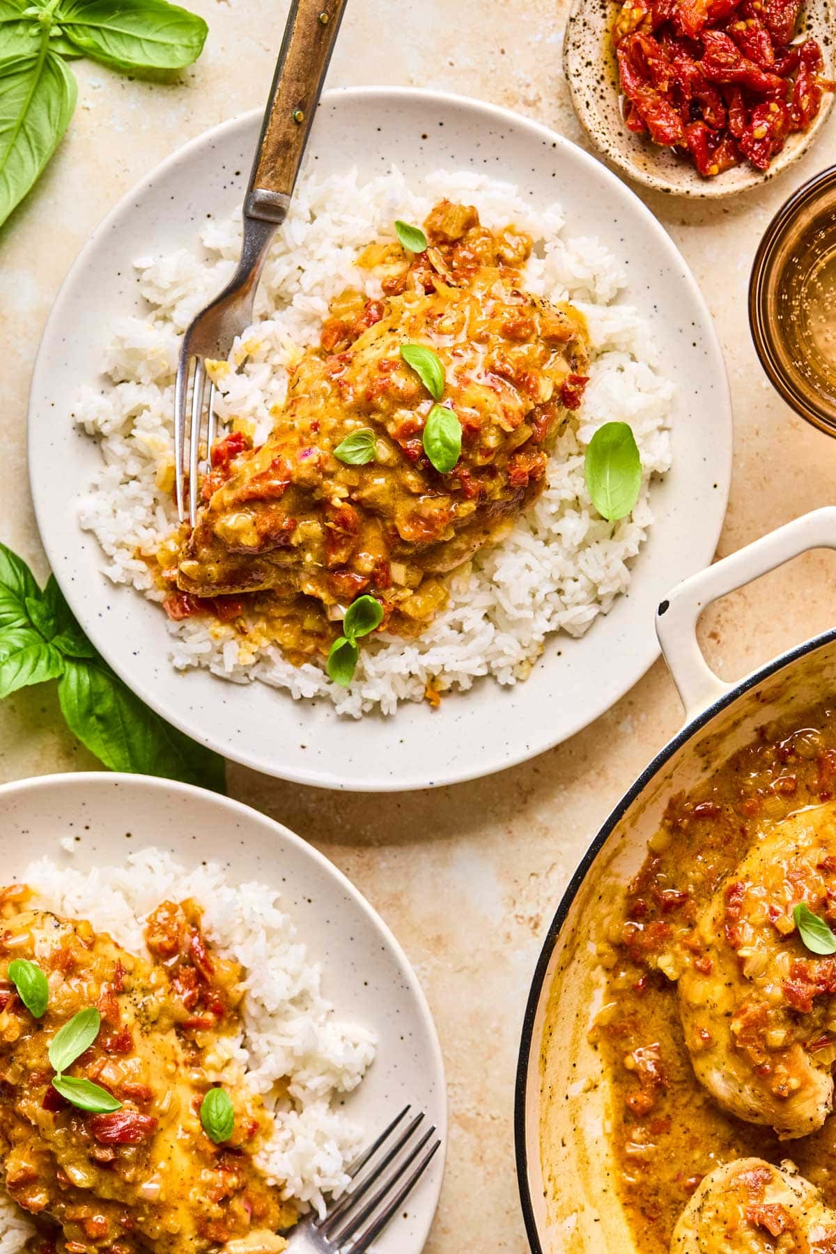 a plate filled with white rice and chicken topped with sun-dried tomatoes and fresh basil