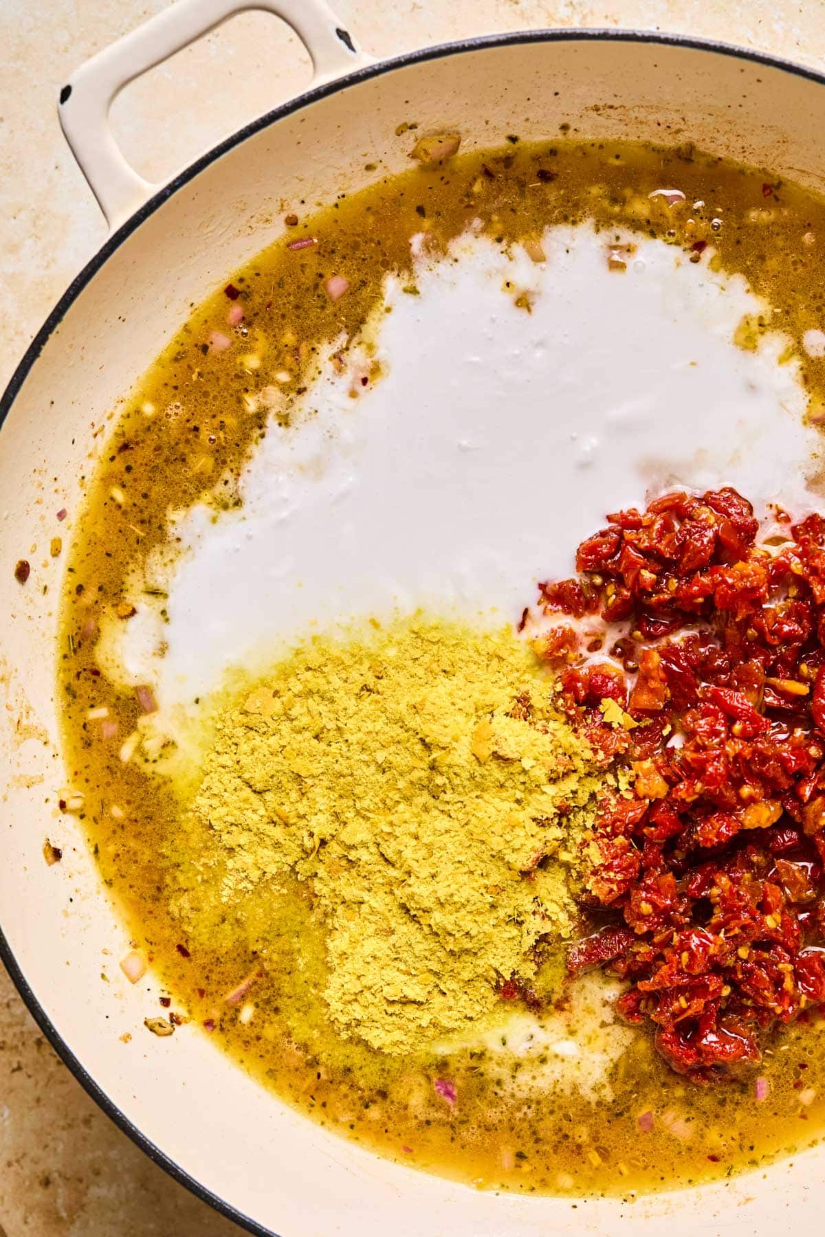 adding coconut milk, sundried tomatoes, and nutritional yeast to the pan to make the marry me chicken sauce