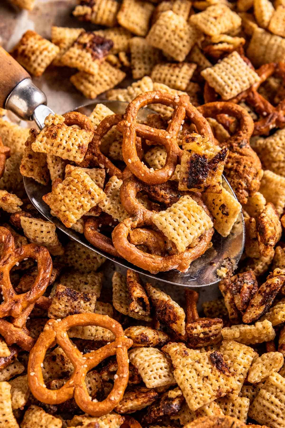 a close up on a large serving spoon filled with a scoop of chex cereal and pretzel twists. 