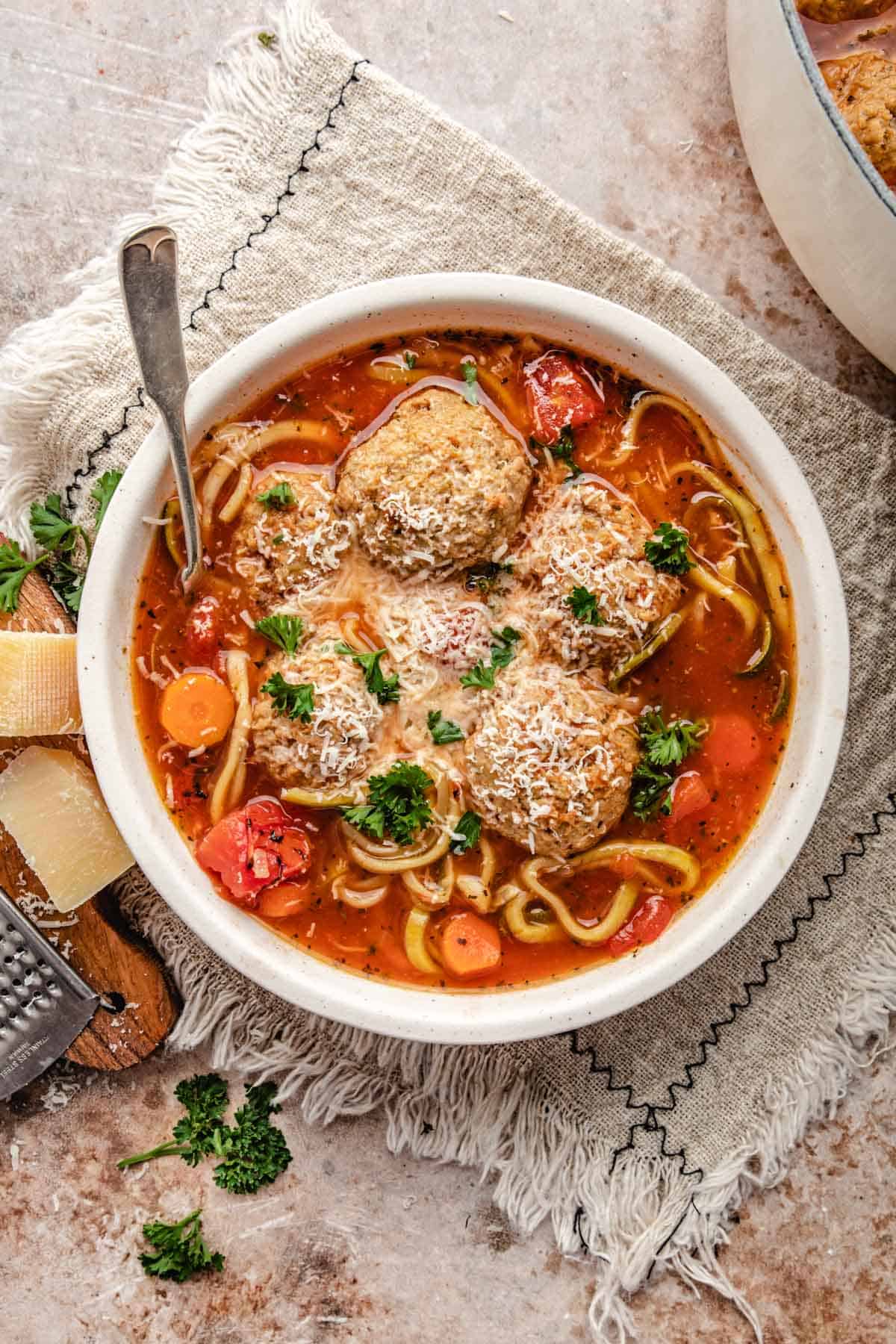 an overhead shot of a white bowl of soup with meatballs and zucchini noodles