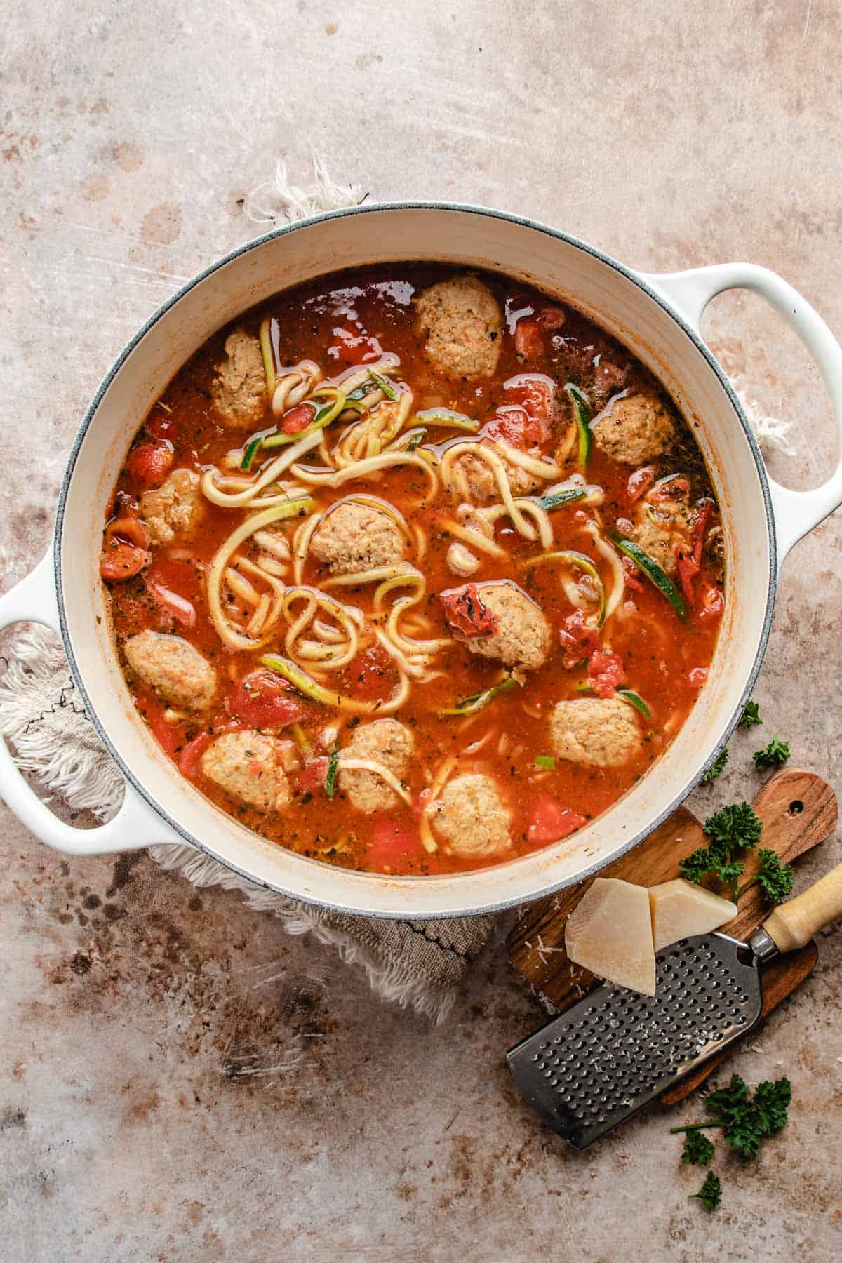 a dutch oven filled with broth, meatballs, and zucchini noodles