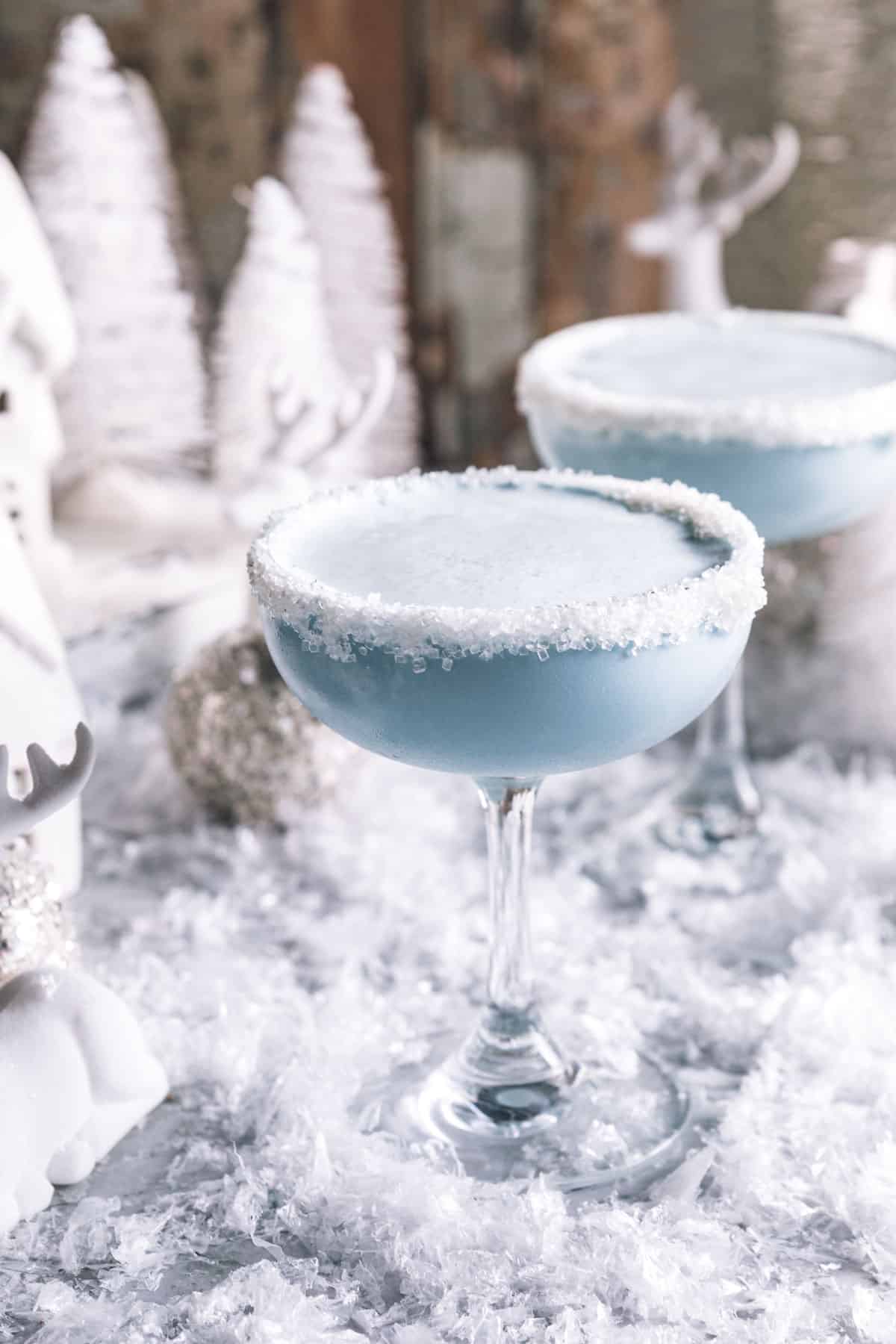 two martini glasses filled with a Jack frost cocktail and rimmed with frosting and sugar sprinkles.