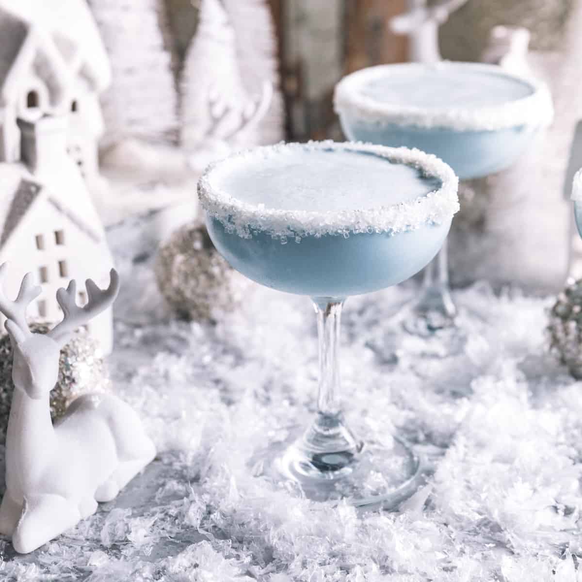 two martini glasses filled with a Jack frost cocktail and rimmed with frosting and sugar sprinkles.