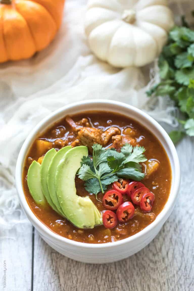 a white bowl of pumpkin chili topped with avocado slices. 