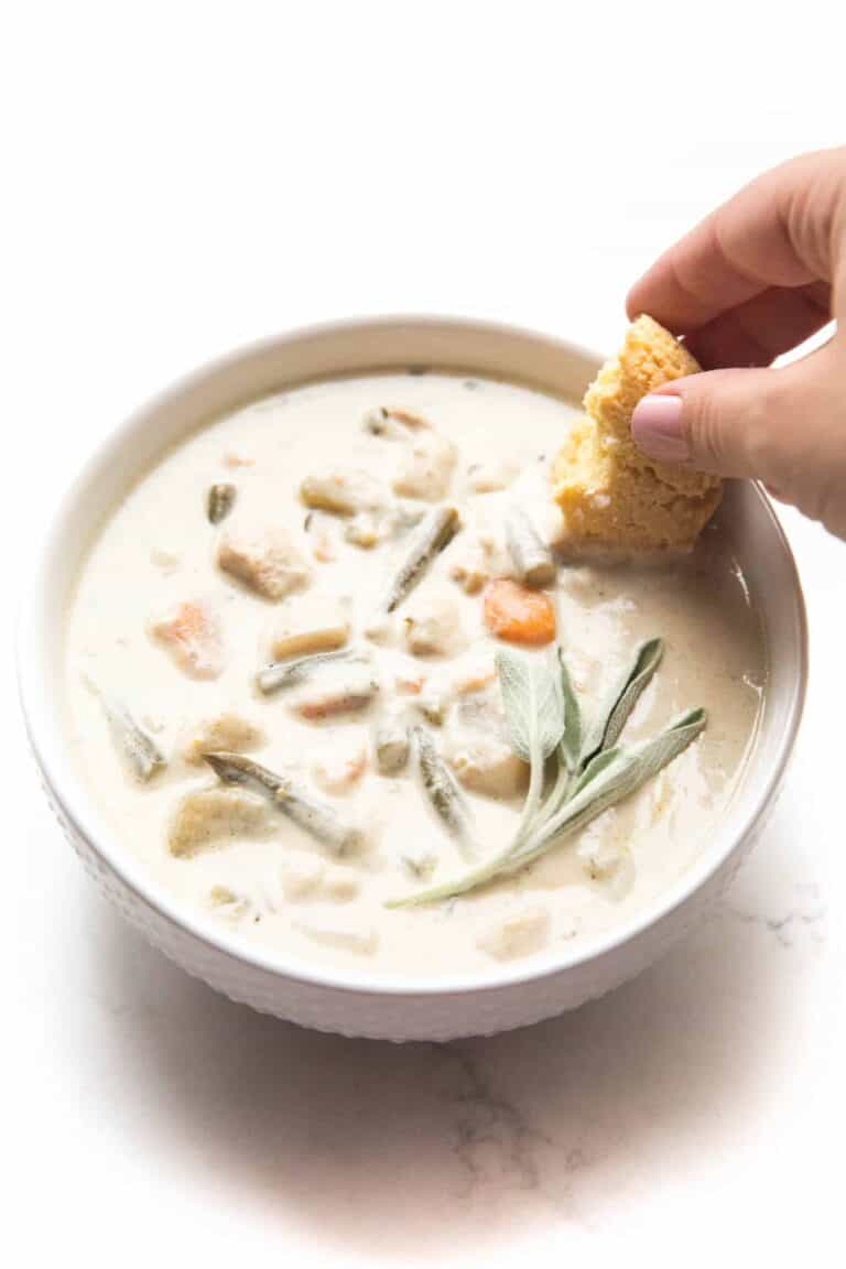 a hand dipping. a biscuit into a bowl of keto creamy chicken chowder.