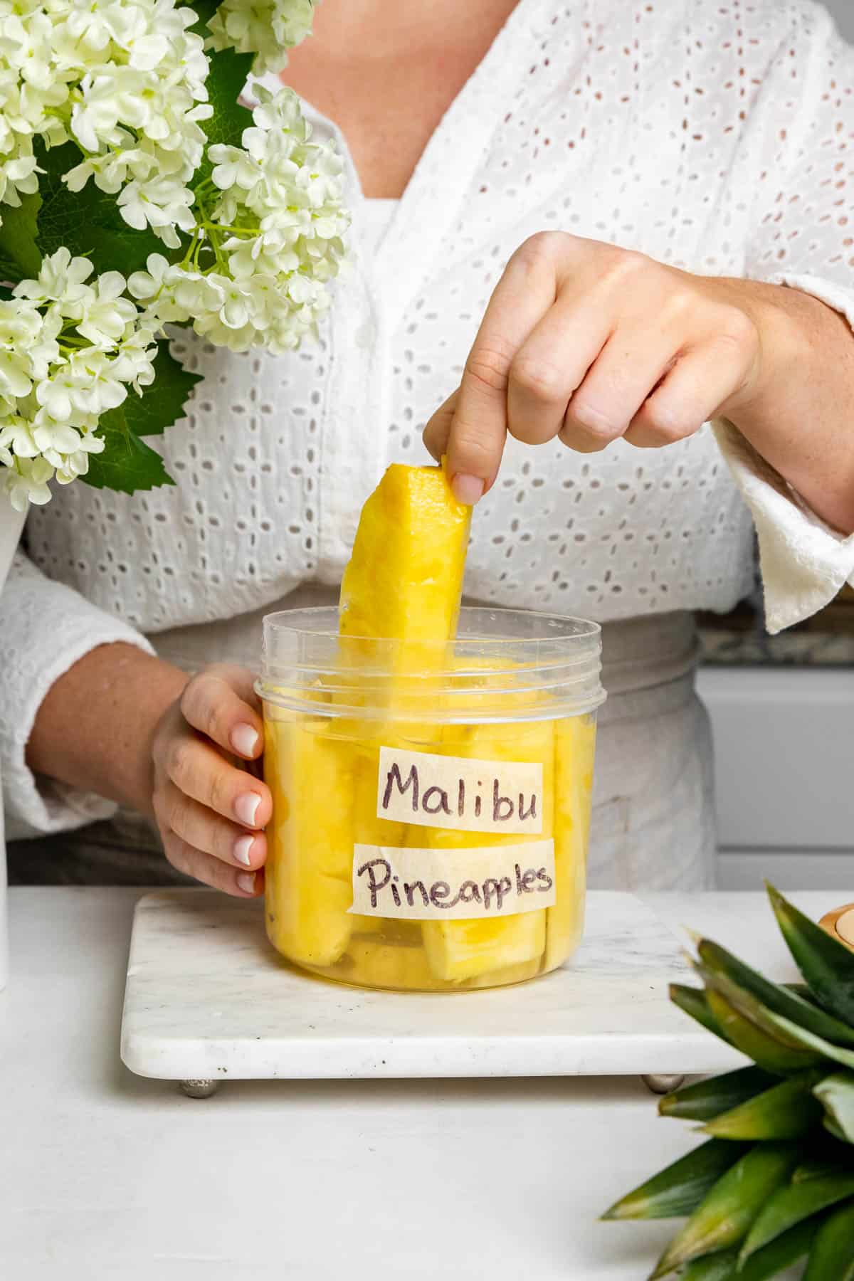 a hand pulling a pineapple spear out of a jar labeled malibu pineapples