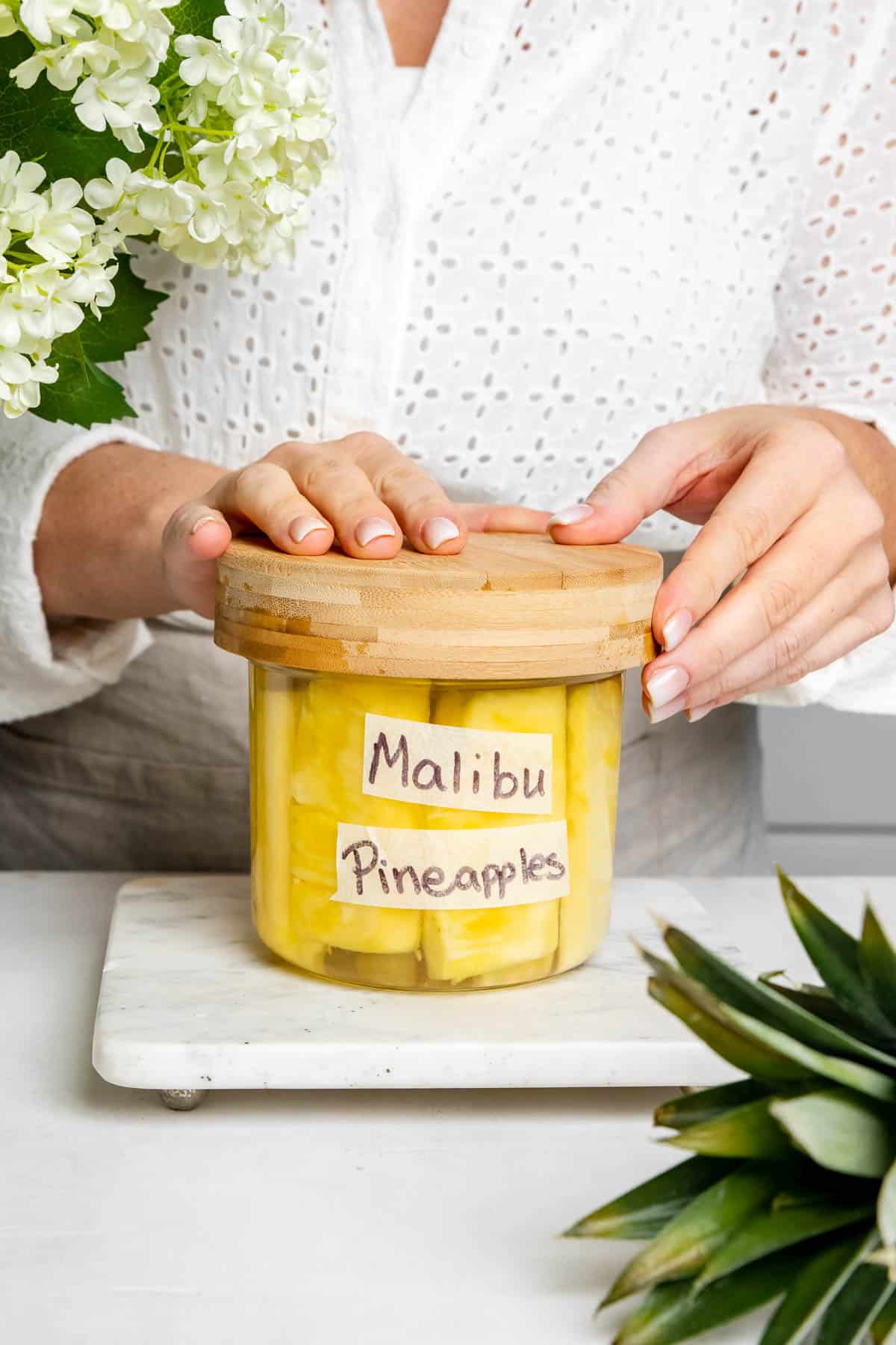 two hands resting on a jar labeled malibu pineapples. 
