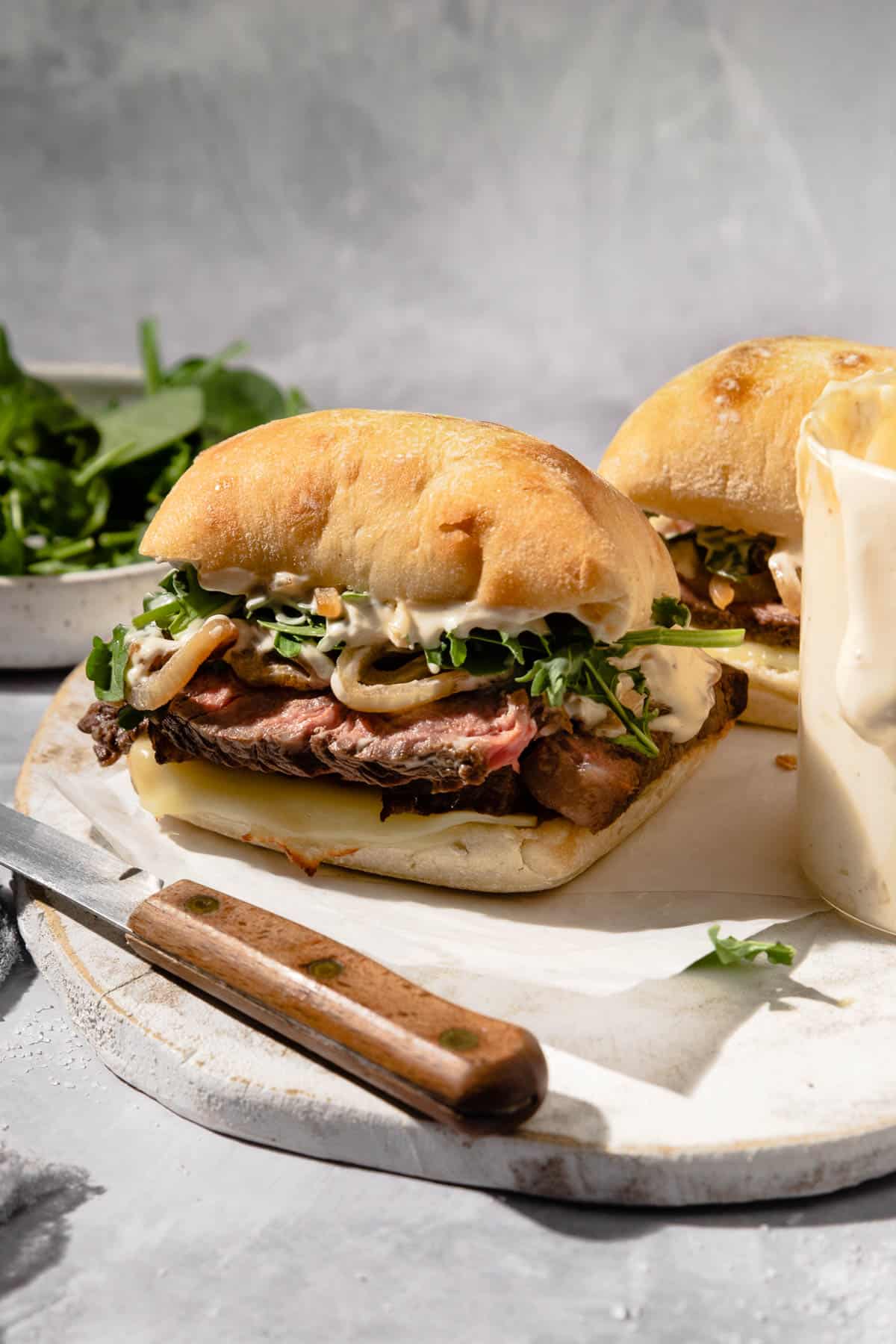 two ribeye steak sandwiches on a wooden cutting board