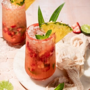 two glasses filled with a strawberry mojito mocktail and garnished with mint and pineapple.