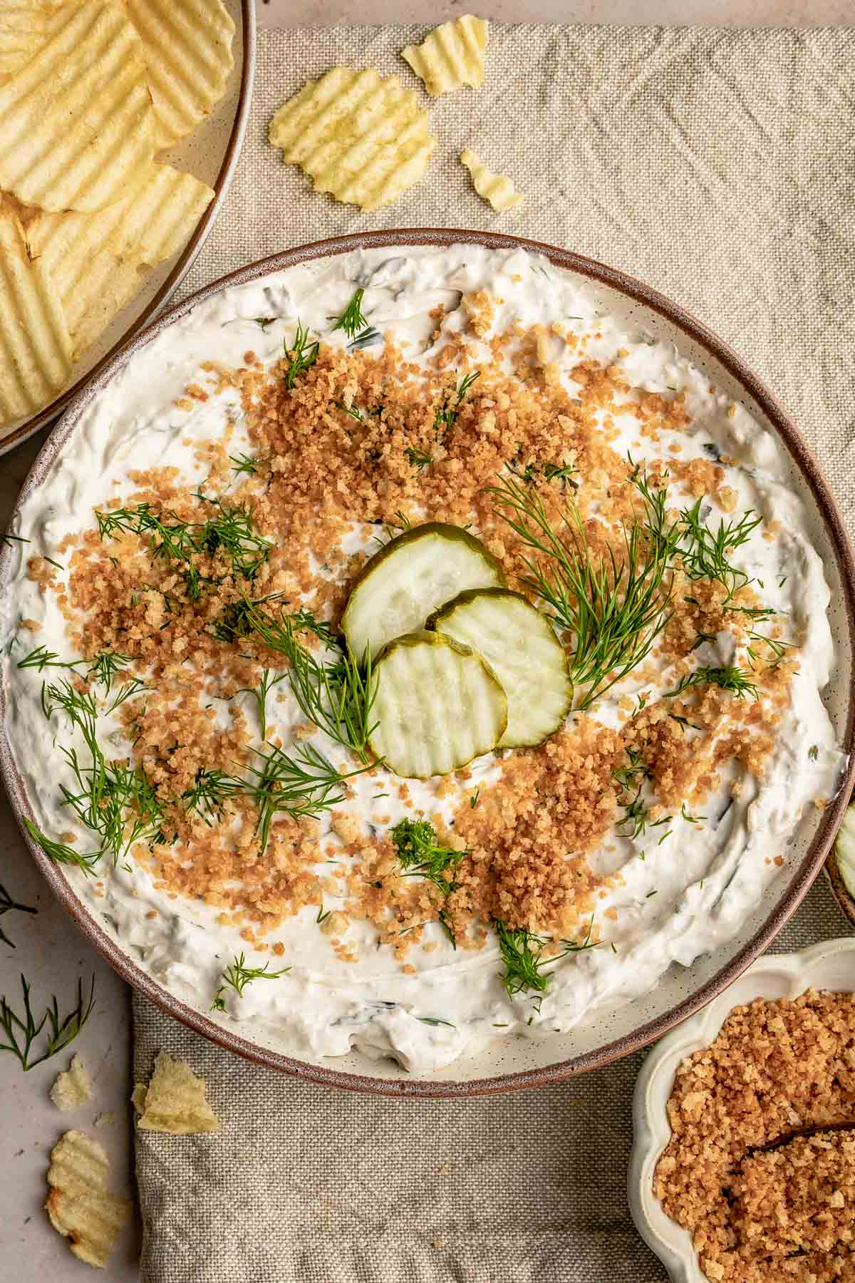 a bowl of fried pickle dip topped with three dill pickles, fresh herbs, and toasted Panko bread crumbs