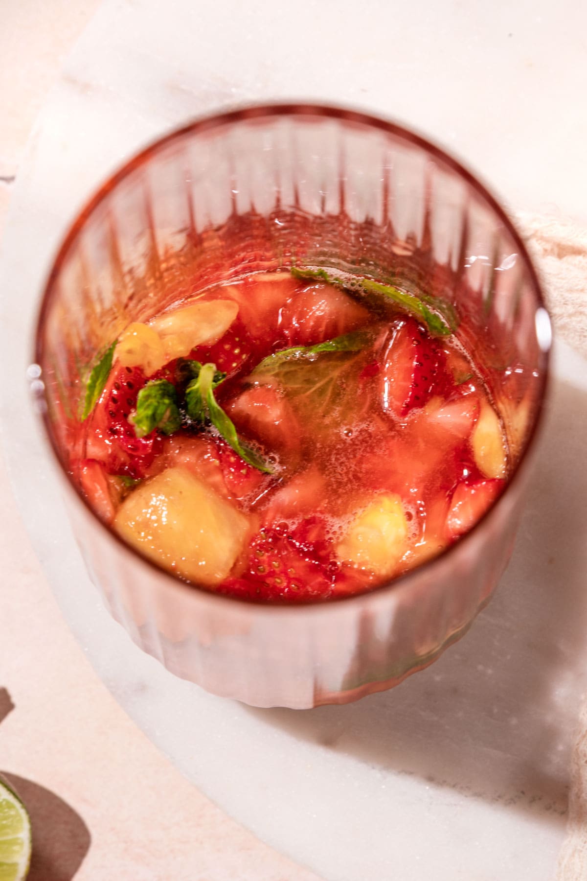an overhead shot of a glass with muddled strawberry, pineapple, and mint.
