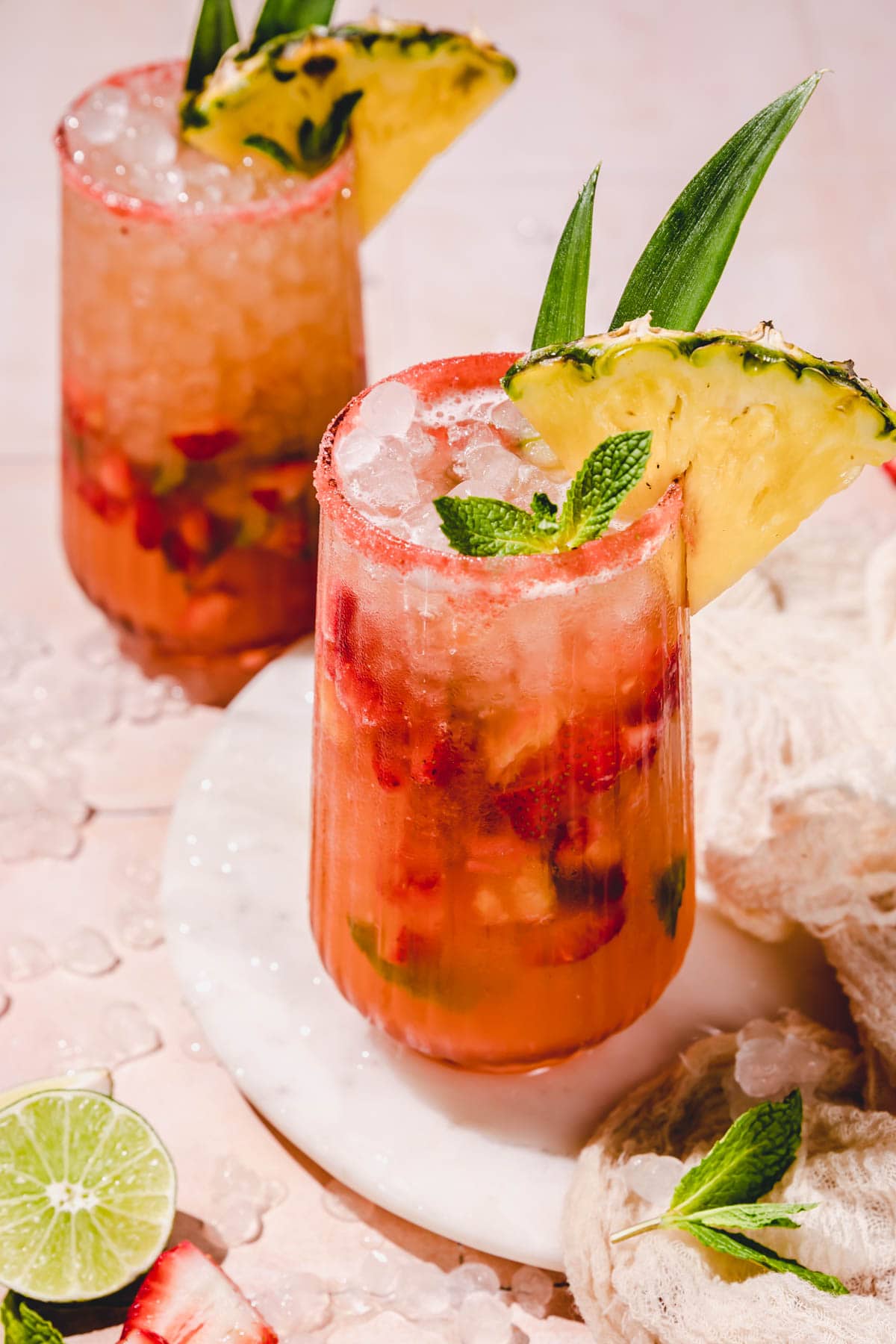 two glasses filled with a stawberry mojito mocktail and garnished with mint and pineapple. 