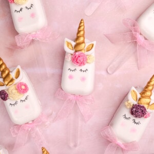 unicorn themed cakesicles on a pink surface